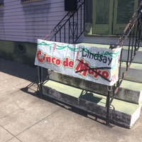 Sign attached to the railings in front of the steps leading up to double doors with text, "Cinco de Mayo" but "Mayo" is crossed out and "Lindsay" is written on the sign. 