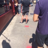 Customers lined up outside a bakery, waiting by heart shaped marks spray painted on the sidewalk that are six feet apart. 