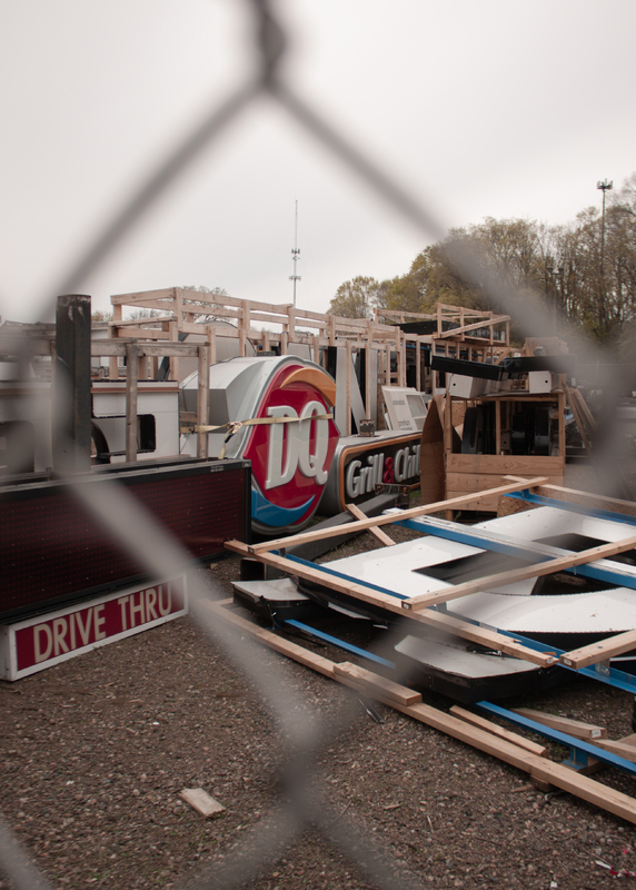 This is a picture taken of various signs for a Dairy Queen restaurant, which have been stored away from the public in a fenced off area during the Pandemic.  