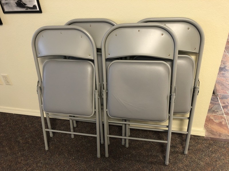 Four grey folding chairs leaning against a wall.