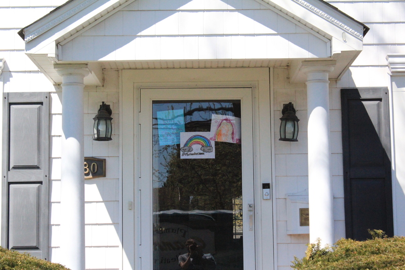 A residential house with three rainbow drawings on the front screen door.