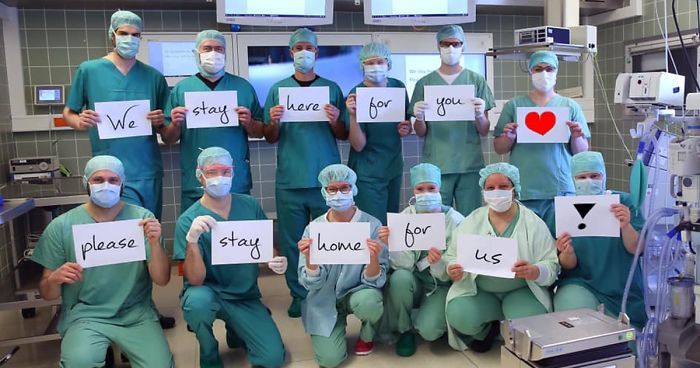 medical staff in scrubs and masks all each hold a piece of paper with a word on it, spelling out "we stay here for you you can stay home for us"