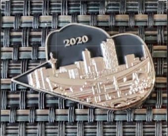 This is a picture taken of a coin which is made in the shape of a hat. It is black, with the image of a city landscape on it and the number "2020" engraved above this image. 