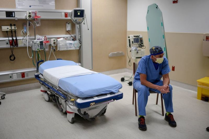 A photo of a healthcare worker sitting next to an empty hospital bed.