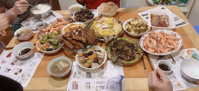 This is a picture of a table covered in multiple different plates of Chinese food, and several people appear to be seated at the table prepared to eat. 