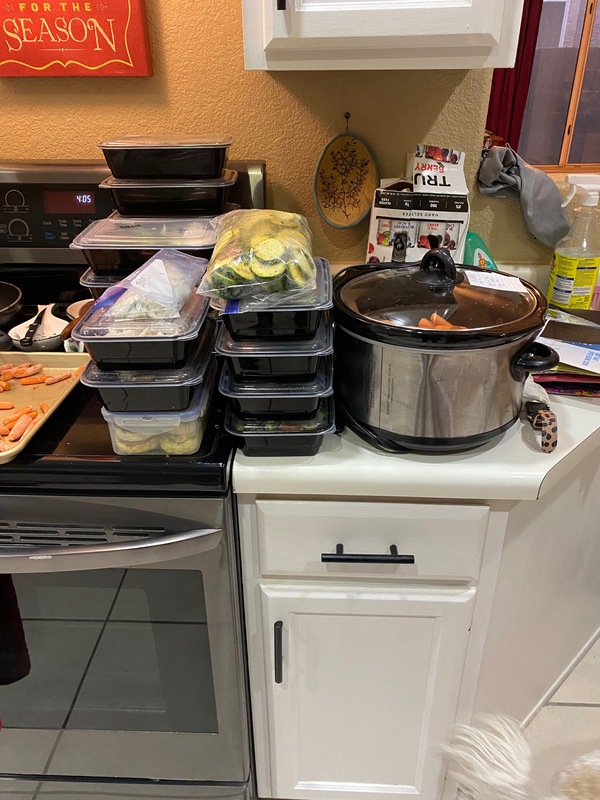 This is a picture taken of a stack of containers which hold different vegetables next to a crock pot on a kitchen counter. 