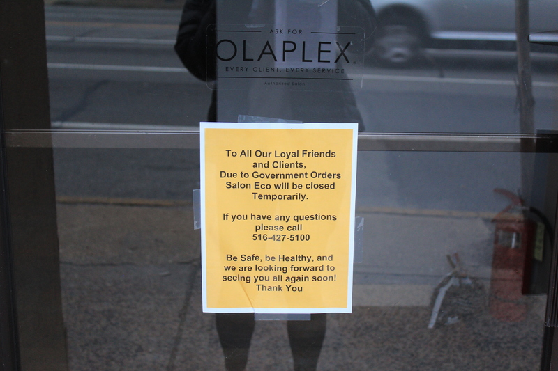 A yellow sign that says: "To all our loyal friends and clients, due to government orders Salon Eco will be closed temporarily. If you have any questions please call 516-427-5100. Be Safe, be healthy and we are looking forward to seeing you all again soon! Thank you!"