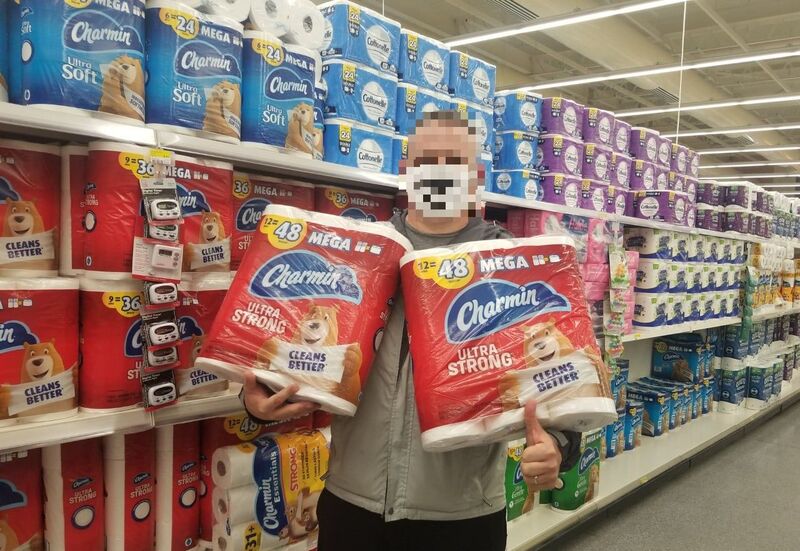 A picture of a man holding toilet paper in a grocery store. 