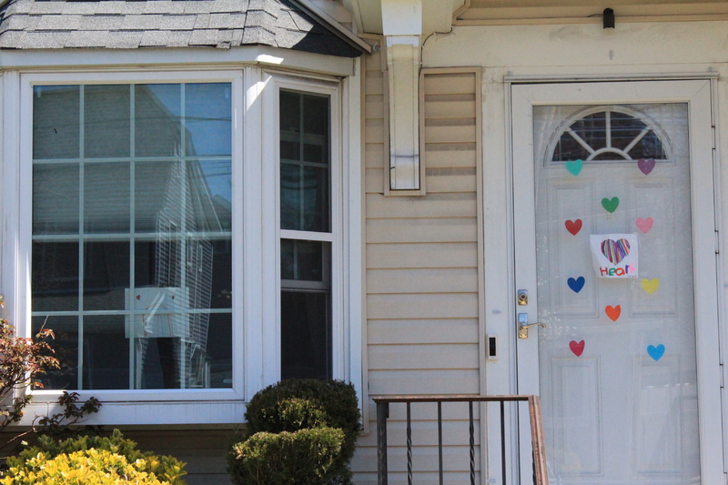 Residential house with a rainbow placed on the front left window, and eleven hearts on the front screen door. 