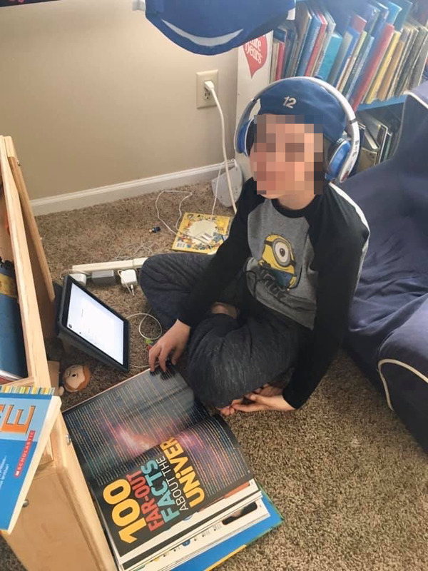 Picture of a young boy reading a book on the floor. His face is blurred. 