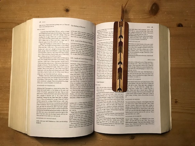 This is a picture of a large book on a wooded table, open in the center with an arrow themed wooden bookmark resting on the pages. 