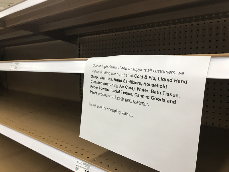 An empty shelf that has a white paper sign taped onto the shelf that reads in black letters "Due to high demand and to support all customers, we will be limiting the number of:" and in bold reads, "Cold & Flu, Liquid Hand Soap, Vitamins, Hand Sanitizers, Household Cleaners (including Air Care), Water, Bath Tissue, Paper Towels, Facial Tissue, Canned Goods and Pasta" in regular font "products to 3 each per customer." 3 each per customer is underlined. At the bottom of the paper sign says "Thank you for shopping with us."