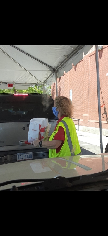 A Chick-fil-A worker walking in front of a car carrying an order wearing a facemask. 