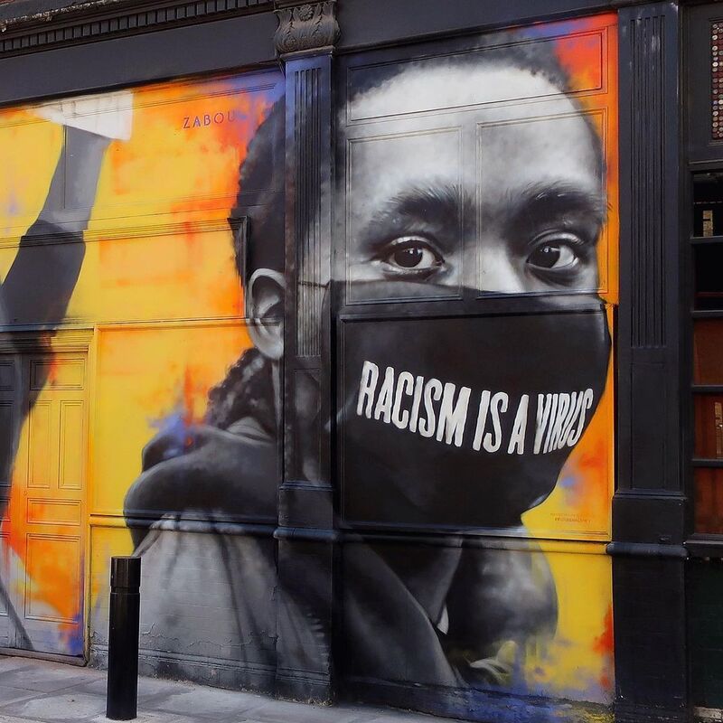 This is a picture of a mural that depicts a black woman wearing a face mask that says "racism is a virus" on it. 