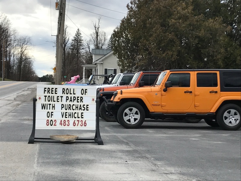 Image of a sign in front of a car dealership which reads free roll of toilet paper with purchase of vehicle. 