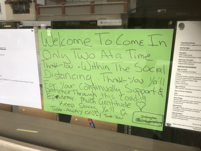 A green sign that is taped on the inside of a restaurant to let its patrons that they are doing take out only and to practice social distancing. 