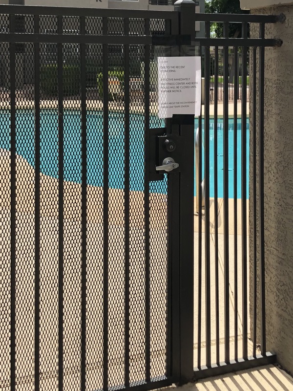 A black gate blocking off entrance to a pool. There's a white paper sign on the black gate that says: 3/16/2020 DUE TO RECENT CONCERNS: EFFECTIVE IMMEDIATELY THE FITNESS CENTER AND BOTH POOLS WITH BE CLOSED UNTIL FURTHER NOTICE. SORRY ABOUT THE INCONVENIENCE GREEN LEAF TEMPE STATION. 