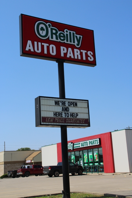 A sign outside an O'Riley's Auto Parts store reading "We're Open and Here to Help".