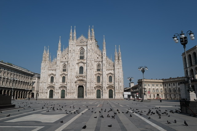 Photo of the Duomo in Milan. The square in front of it is empty except for birds. 