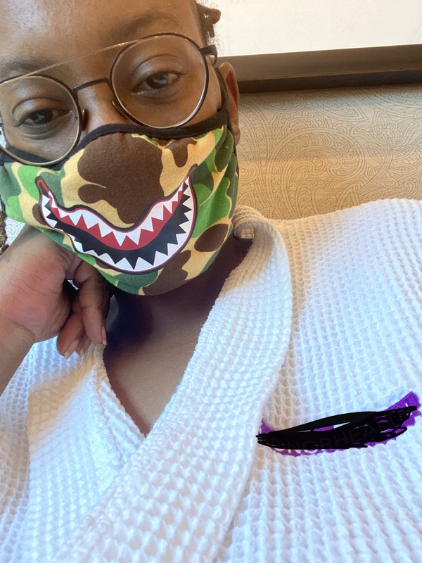 A picture taken of a woman wearing glasses, who is also wearing both a mask and a hospital uniform. 