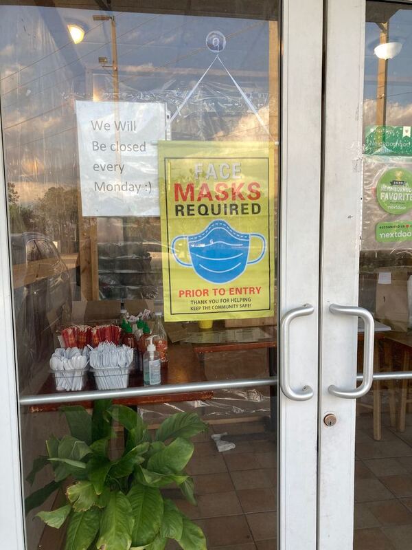 This is a picture taken of several signs posted in the window of a storefront. They read "Face masks required prior to entry. Thank you for helping keep the community safe!", and "We will be closed every Monday :)". 
