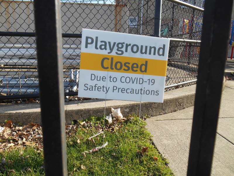 A yard sign that says: "Playground Closed Due to COVID-19 Safety Precautions". 