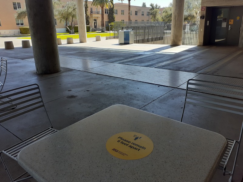 Public table and chairs outdoors.  A sticker on the table reads "please remain six feet apart".