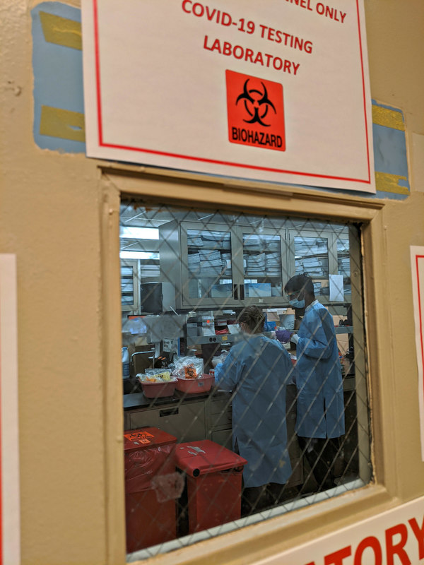Closed biohazard laboratory with two medical professionals testing COVID-19 specimens.  