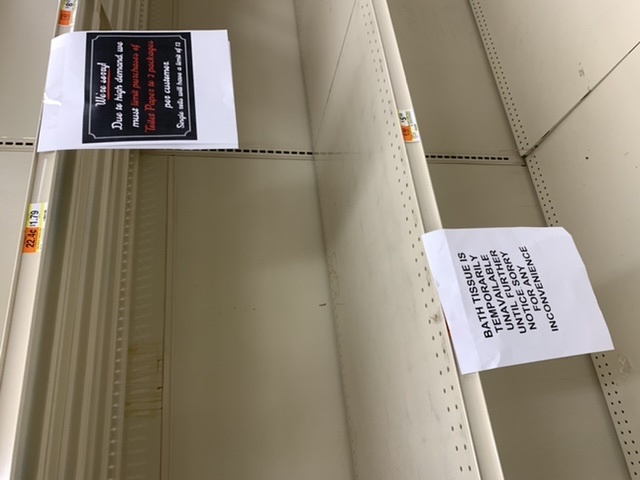 Empty shelves in a supermarket that has signs saying they toilet paper temporarily unavailable. 