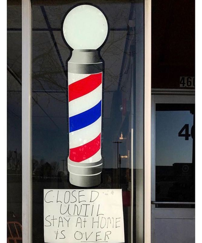 Barber shop window with a window decal of a barber shop pole and sign with text, "CLOSED UNTIL STAY AT HOME IS OVER"