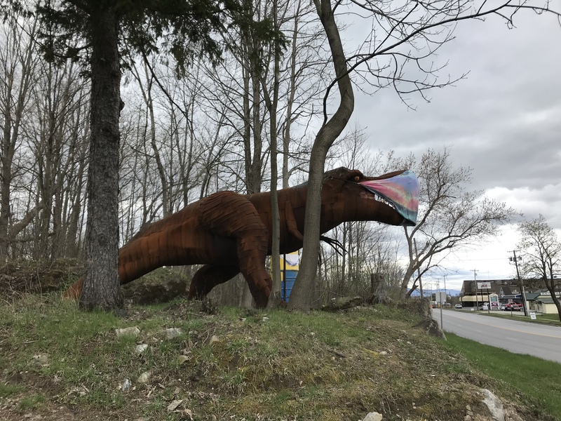 A statue of a dinosaur with a mask on in the woods. 