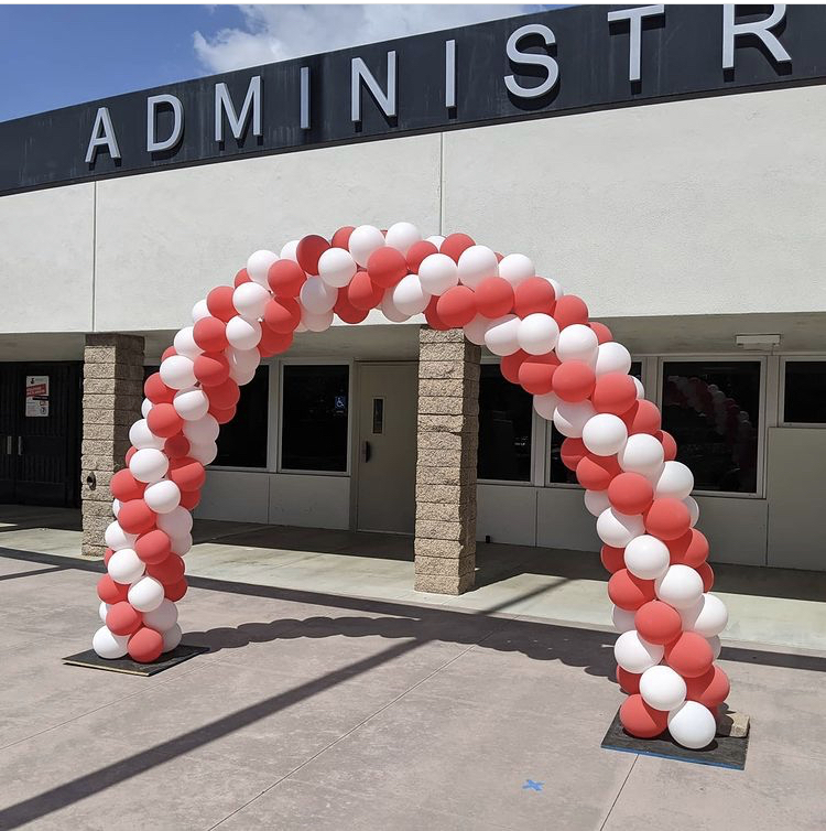 This is a picture of a large arch made out of red and white balloons, which is placed in front a building which has a sign on it that reads "administration". 