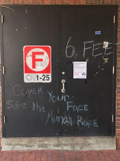 Graffiti on a door that reads "Cover your face, Save the Human Race".