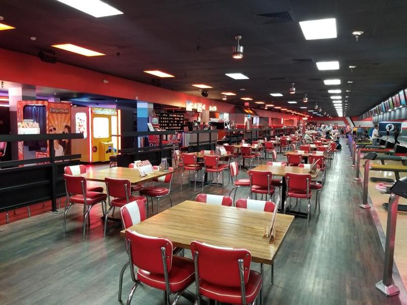 A bowling alley with empty red and white tables and chairs going off into the distance. 