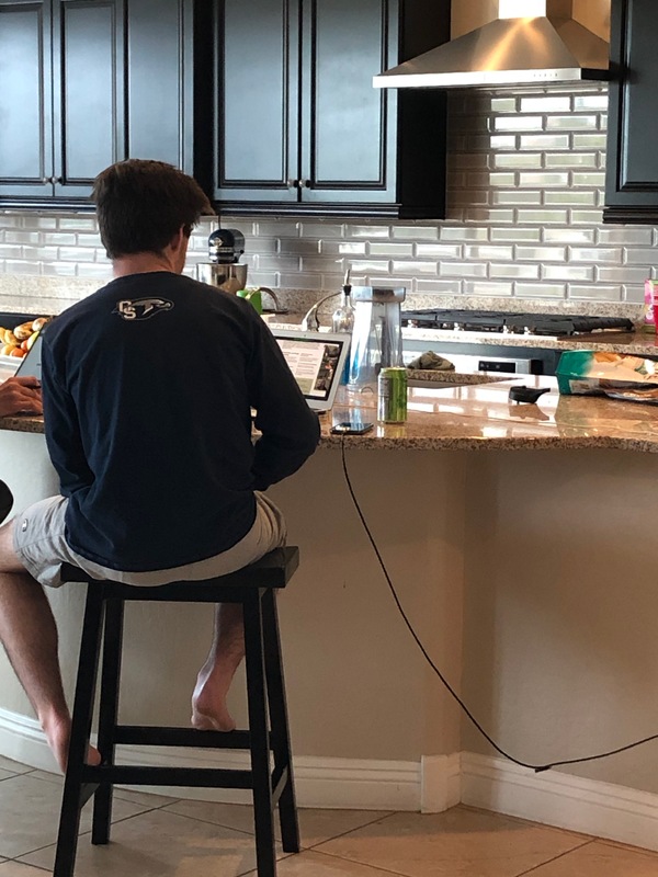 A young man sitting at a kitchen counter attending a virtual orientation for University.