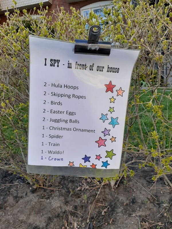 This is a picture taken of a sign set up in front of a persons house. It reads: "I SPY- in front of our house: 2 hula hoops, 2 skipping ropes, 2 birds, 2 Easter eggs, 2 juggling balls, 1 Christmas ornament, 1 spider, 1 train, 1 waldo, 1 crown."