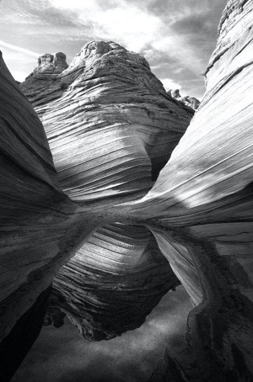 This is a black and white photo of the image of a canyon reflecting from a pool of water at its bottom. 