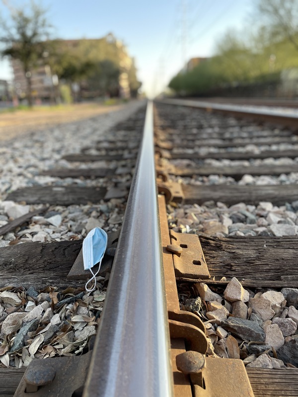 This is a picture of a discarded cloth mask resting on a series of train tracks. 