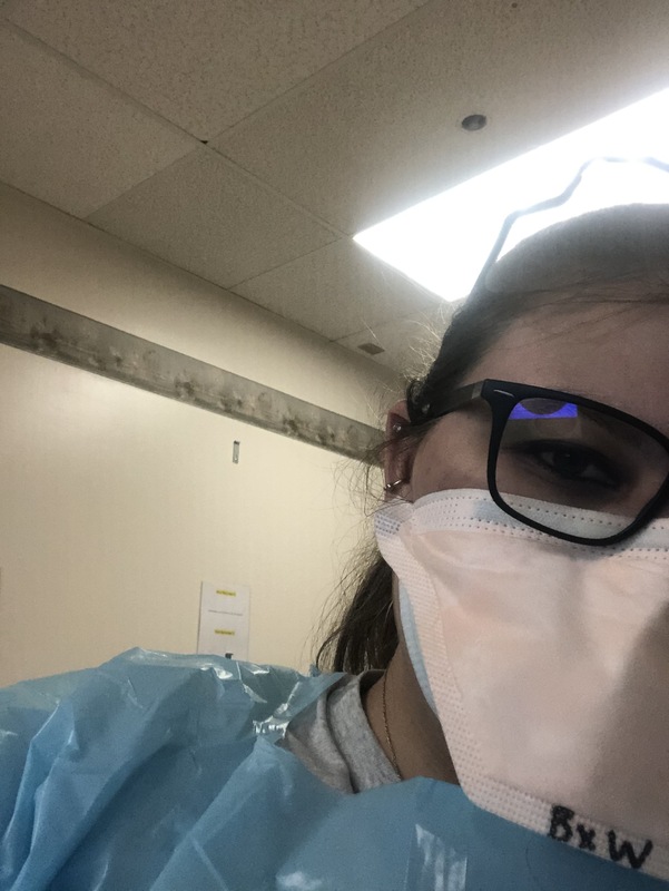 This is a picture of a girl wearing protective clothing and a face mask labeled "BxW" looking into the camera. She is wearing glasses. 