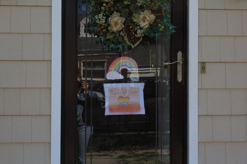 A residential house with a rainbow with a message under it that says "there is still hope" on the front screen door.