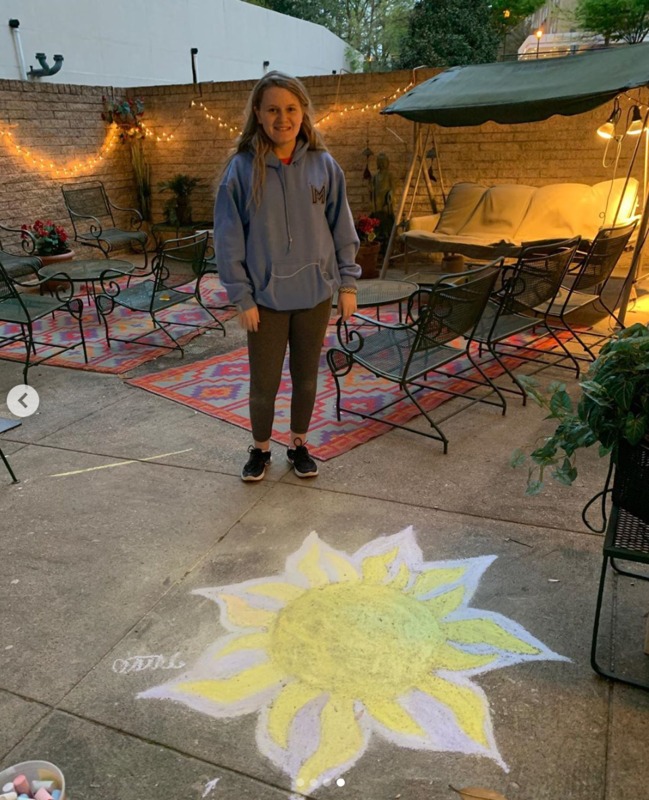 Photo of a woman standing behind a chalk drawing of the sun.