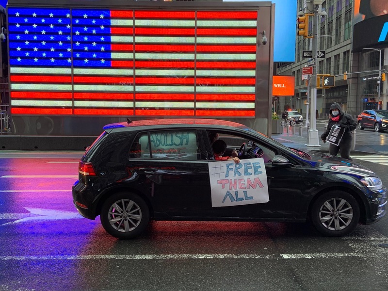 A person in a car holding a sign in front of an American flag. 