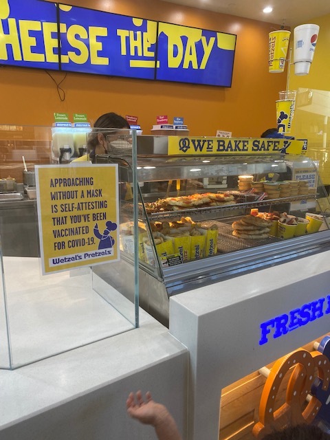 This is a picture of a counter at a Wetzel's Pretzels restaurant, where a sign urges people to wear a face mask. 
