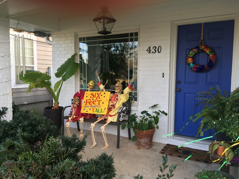 Front porch with Halloween decorations.  Two skeletons hold sign that says, "Six Feet When Possible, Y'all!".
