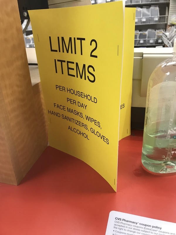 A yellow paper sign on a shelf that says: LIMIT 2 ITEMS PER HOUSEHOLD PER DAY FACE MASKS, WIPES, HAND SANITIZER, GLOVES, ALCOHOL.