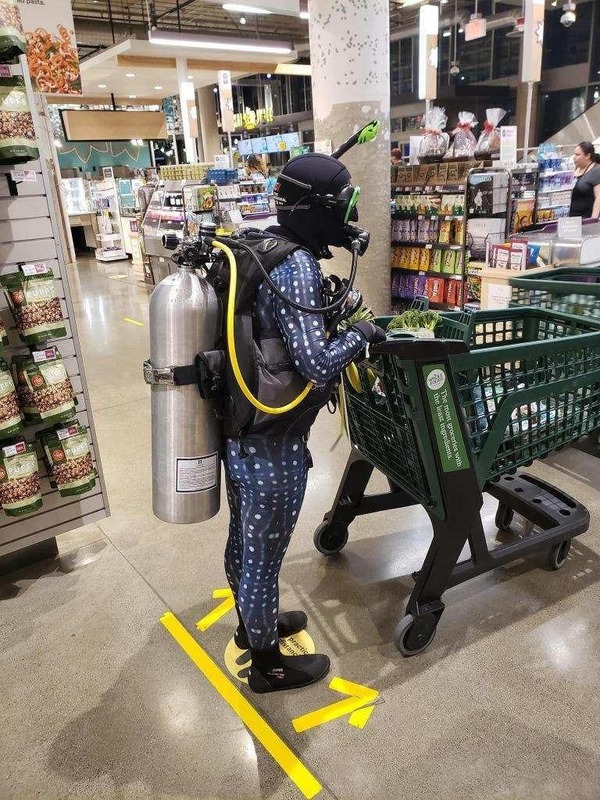 A person wearing a scuba diving suit and pushing a shopping cart at a grocery store. 