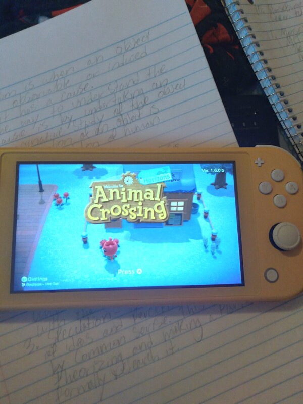 This is a picture of a person's Nintendo Switch resting on a notebook, with the logo for the game Animal Crossing showing on the screen. 