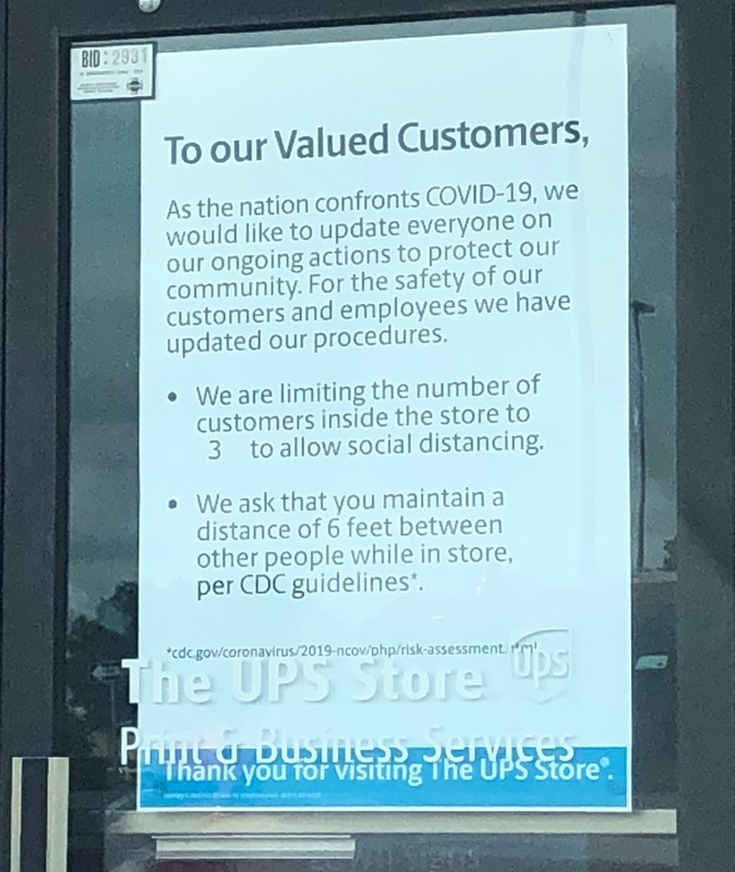 Image of a sign on the door of the UPS store which reads to our valued customers, as the nation confronts Covid-19, we would like to update everyone on our ongoing actions to protect our community. For the safety of our customers and employees we have updated our procedures. We are limiting the number of customers inside the store to three to allow social distancing. We ask that you maintain a distance of six feet between other people while in store, per CDC guidelines.