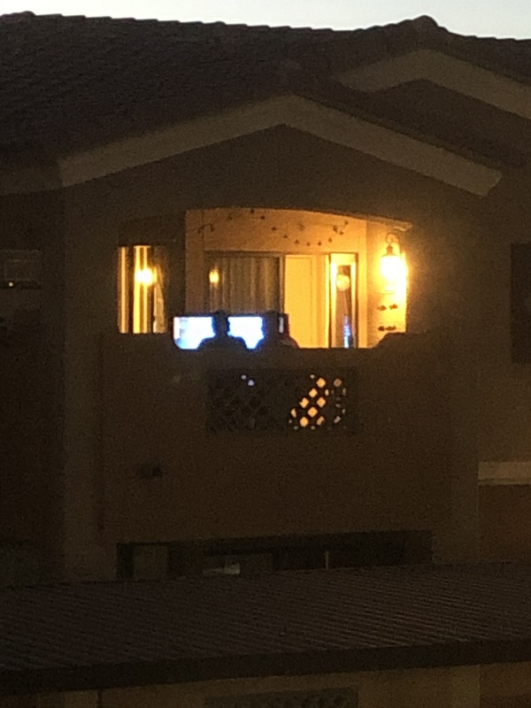 Two men sit on a darkened balcony at night, watching the Super Bowl on television.