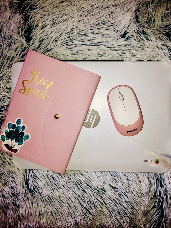 A pink journal and a computer mouse on top of a computer. All of these items are laying on a shag rug. 
